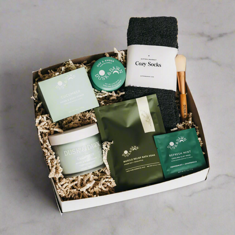 Gift box with bath products including a candle, face mask, and socks on a white background